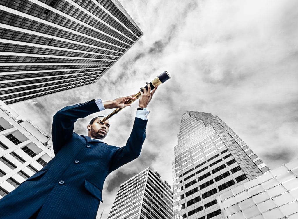 businessman holding telescope with clouds and tall buildings in background